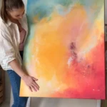 slečna drží abstraktní žluto-červeno-modrý obraz