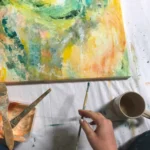 kousek abstraktního obrazu a štetec v ruce s barvou