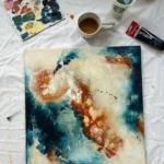 abstraktní hnědo-modrý obrazna zemi s baravmi a hrnkem