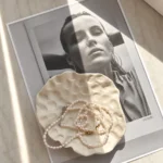 A4 stránka černobílé fotky s ženou a na tom béžová miska ve které jsou šperky z perel