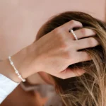 žena s rukami za hlavou, která má na sobě prstýnek a náramek z perel